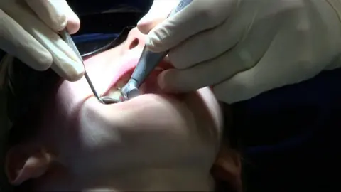 Dentist with mirror and drill in a patient's mouth