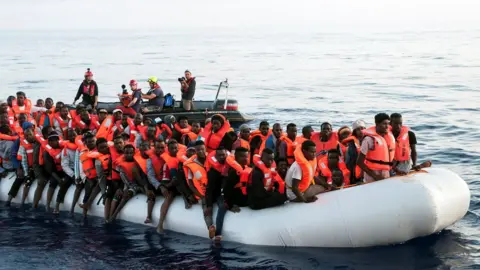 Reuters Migrants are seen in a rubber dinghy as they are rescued by the crew of the Mission Lifeline rescue boat in the central Mediterranean Sea, 22 June 2018