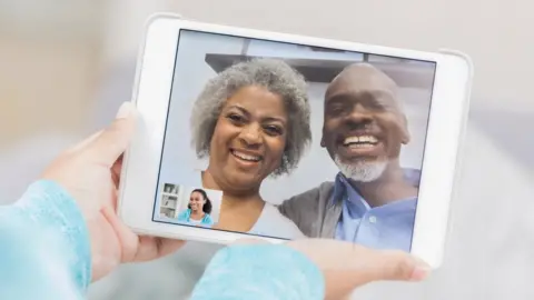 Getty Images A stock photo shows two older people on a tablet, calling a younger person