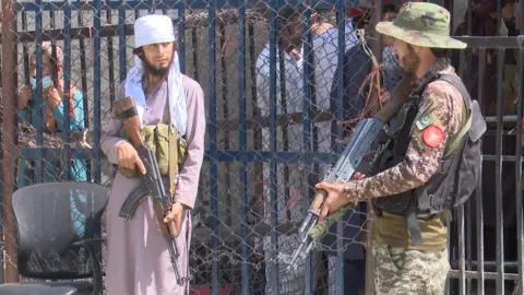 BBC An armed Taliban fighter (left) and an armed Pakistani soldier at the Torkham crossing on the Pakistani-Afghan border