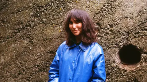 Sam Buchan-Watts Rebecca Birell standing against a wall in a blue rain jacket
