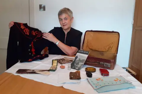 Judith Rhodes Judith Rhodes with her mother's suitcase and some of the belongings she brought with her
