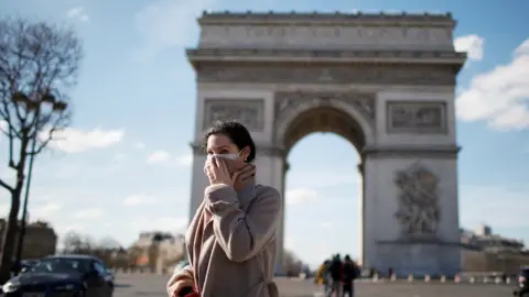 Reuters A woman wearing a protective mask walks near the Arc de Triomphe in Paris, 15 March