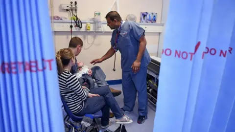 AFP/Oli Scarff via Getty Images A doctor talking to a couple with their baby