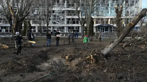 AFP Bystanders look at a crater next to an educational building damaged the previous day by a missile strike in Kyiv