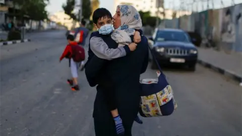 Reuters A Palestinian woman carrying her son evacuates after their tower building was hit by Israeli airstrikes, amid a flare-up of Israeli-Palestinian violence, in Gaza City May 12, 2021.