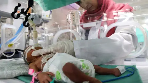 Reuters A medical worker assists a premature Palestinian baby lying in an incubator at the maternity ward of al-Shifa Hospital, in Gaza City (22 October 2023)