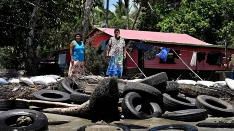 Getty Images Resident Lavenia McGoon (R) with a family member standing past a makeshift seawall of old rubber car tyres to prevent erosion, outside her beachfront house at a village in the coastal town of Togoru, some 35 kilometres from Fijis capital city Suva.