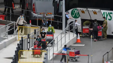 Getty Images Recently returned passengers wearing face masks take their luggage to a quarantine hotel in Sydney