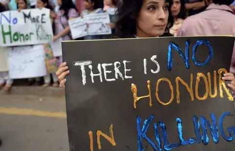 Getty Images A woman carries a sign at a 2014 protest reading: "There is no honour in killing"