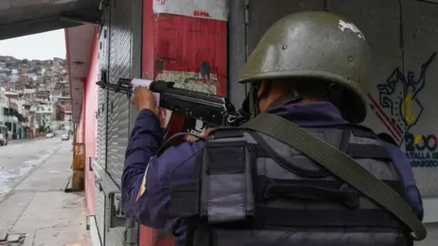 AFP VIA GETTY IMAGES A member of the Bolivarian National Police aims at a possible target after clashes with alleged members of a criminal gang at the Cota 905 neighbourhood, in Caracas on July 9, 2021.