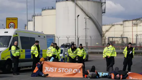 PA Media Police officers look at activists from Just Stop Oil taking part in a blockade at the Kingsbury Oil Terminal, Warwickshire