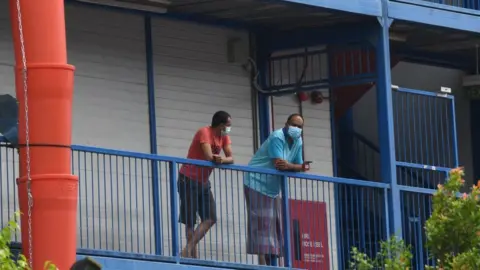 Getty Images Migrant workers wearing face masks as prevention for the spread of the COVID-19 coronavirus look out from a quarantined dormitory building in Singapore on 20 May 2020.