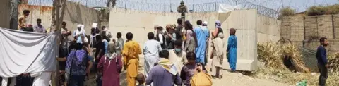 Getty Images People crowd a gate at Kabul's airport