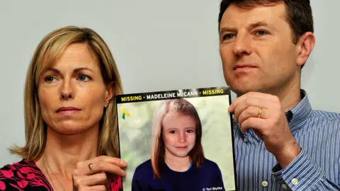 PA Media Gerry and Kate McCann whose daughter Madeleine disappeared from a holiday flat in Portugal in 2007 at a press conference in London where they hold an image of what Madeline might look like as an older girl. A German prisoner has been identified as a suspect in the disappearance of Madeleine, detectives have revealed.