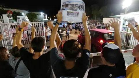 Getty Images Apple Daily journalists hold freshly-printed copies of the last edition while acknowledging supporters gathered outside their office