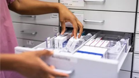 Getty/Luis Alvarez Close-up of a pharmacist searching for prescription medicine in storage rack.