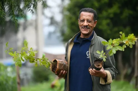 AFP An Ethiopian man poses holding saplings.