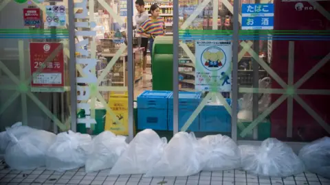 AFP A shop in Tokyo has taped up windows and bags filled with water at its entrance in preparation for Typhoon Hagibis on 12 October.