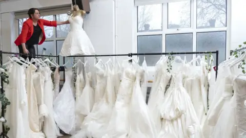 PA Media Sidcup charity shop manager Sally Todd surrounded by donated wedding dresses