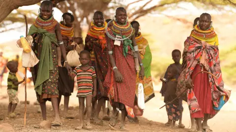 AFP Villagers, mostly women and children, gather under a tree in Purapul village, Loiyangalani area, during World Vision-supported health interventions that help communities tackle malnutrition and other health problems caused by drought, in northern Kenya - Tuesday 12 July 2022