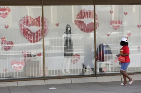 EPA A woman walks past a shop window decorated with illustrations of kissing lips in Harare, Zimbabwe - Sunday 13 February 2022