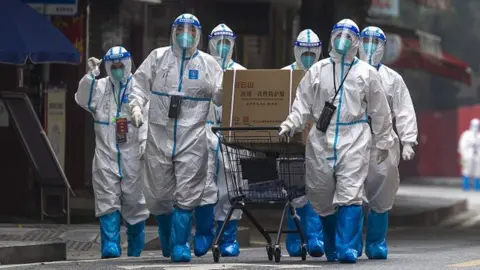 Getty Images Workers in PPE walk by a residential block under COVID-19 lockdown in Guangzhou in south China's Guangdong province on Thursday, November 10, 2022.