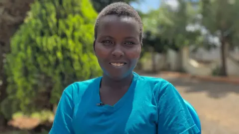 BBC A woman in a blue t shirt smiles at the camera