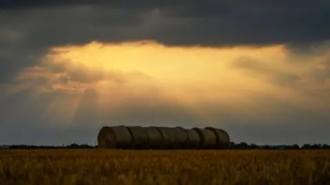 AFP/Getty The sun shines through dark clouds onto large straw bales in a field