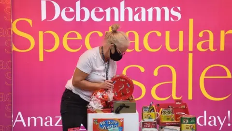 Getty Images A shop assistant adjusts a window display in Debenhams in front of a sale sign