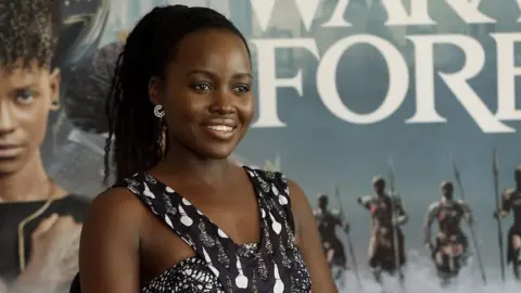 Lupita Nyong’o in front of Black Panther; Wakanda Forever poster