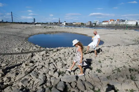 Reuters A family walks next to a puddle in the partially dried riverbed of Rhine, in front of the skyline of Dusseldorf, Germany