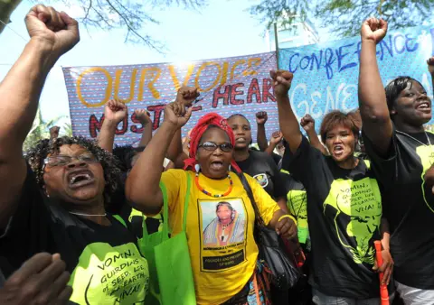 AFP A group of women farmers with their fists raised, carrying protest banners