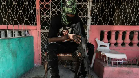 Getty Images A man sits with a machine gun in Port-au-Prince