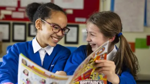 PA Media Adele Amour (left) and Emily Pollara from Northside Primary School laugh at each other while they hold Beano