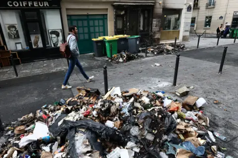 YVES HERMAN/REUTERS A man walks past a burnt store and damages in a street the day after clashes during protests over French government's pension reform in Paris, France, March 24, 2023.