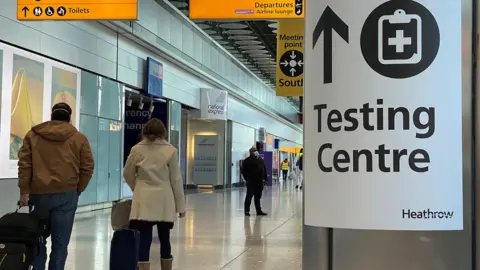 Reuters Travellers walking past a testing centre sign at Heathrow Airport