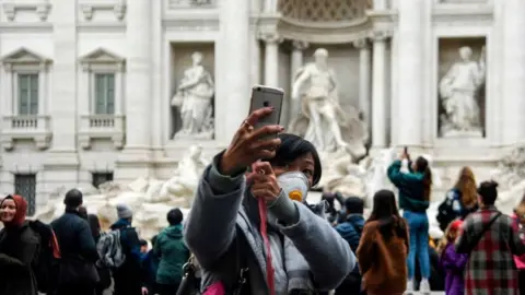 Getty Images A Chinese tourist by the Trevi fountain in Rome, taking a selfie while wearing a face mask