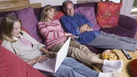 Grandparents watch television while granddaughter uses her laptop