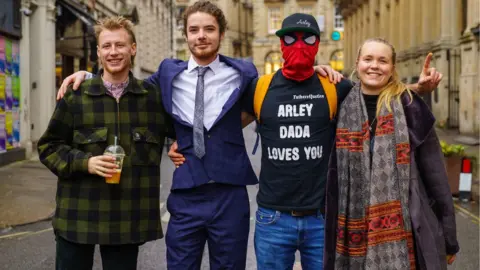 Ben Birchall/PA Media Milo Ponsford, left, Sage Willoughby, second left, Jake Skuse, second right in mask, and Rhian Graham right, accused of criminal damage over the toppling of the statue of slave trader Edward Colston, outside Bristol Crown Court