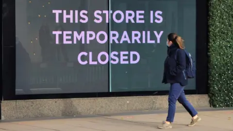 Getty Images Woman in mask walks past shop sign saying 'This store is closed'