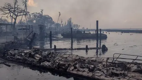 Reuters A charred boat lies in the scorched waterfront after wildfires fanned by the winds of a distant hurricane devastated Maui's city of Lahaina, Hawaii, U.S. August 9, 2023.