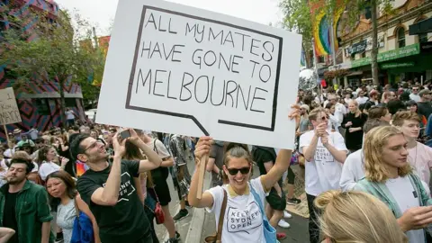 Getty Images A woman at a protest holds a sign saying "all my mates have gone to Melbourne"