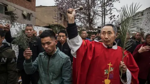 Getty Images Chinese Catholic deacon sprays holy water on worshippers at the Palm Sunday Mass during the Easter Holy Week at an 'underground' or 'unofficial' church on April 9, 2017 near Shijiazhuang, Hebei Province, China.