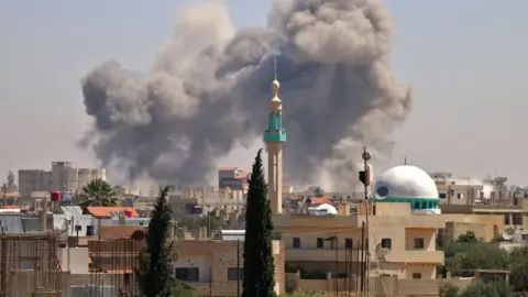 AFP Smoke rises from the rebel-held town of Nawa, north of Deraa, Syria, during air strikes by pro-government forces (27 June 2018)