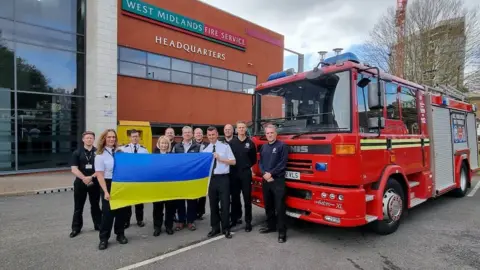 West Midlands Fire Service Staff holding up a Ukraine flag in front of the fire engine being donated