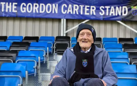 Little Oakley FC Gordon Carter sitting in the stand named in his honour