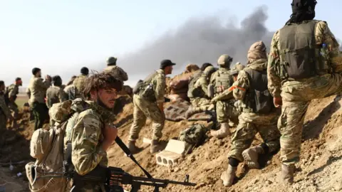 AFP Turkish-backed Syrian rebels and Turkish soldiers watch as smoke rises from the Syrian town of Ras al-Ain on 12 October 2019