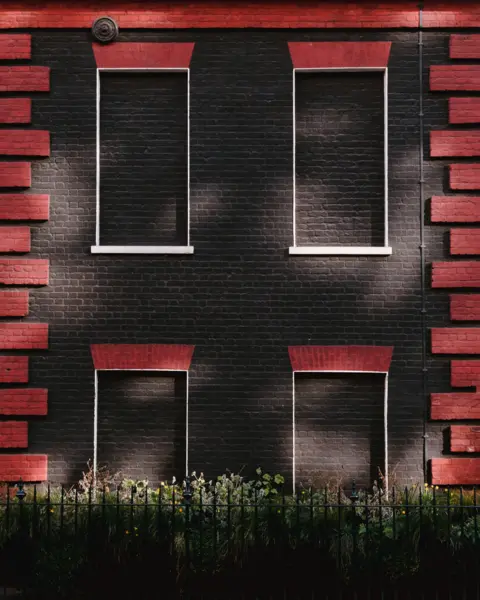 Andy Billman Four blocked windows on a building painted black and red, on Davies Street, London