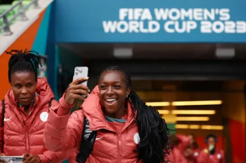 Hannah Mckay/Reuters Michelle Alozie smiling, whilst holding up her phone in the football stadium.